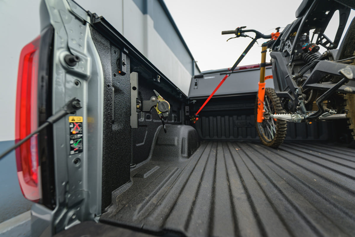 Dirt bike secured with Ultimate Retractable Ratchet Straps in a GMC Sierra bed, viewed from the tailgate